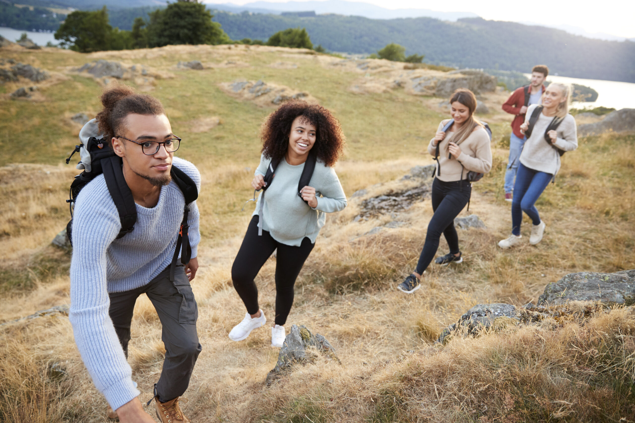 A multi ethnic group of five young adult friends smile while climbing to the summit during a mountain hike, close up