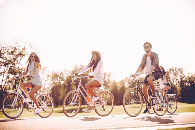 Spending nice summer day together. Group of young people riding bicycles along a road and looking happy
