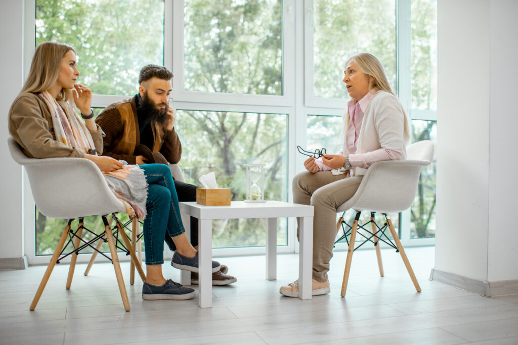 Young couple having misunderstandings during the psychological counseling with senior female psychologist in the office