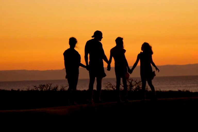 Silhouettes of four people holding hands and walking along the shoreline at sunset, reflecting the joy, freedom, and connection that can come after completing a medical fentanyl detox program and beginning recovery.