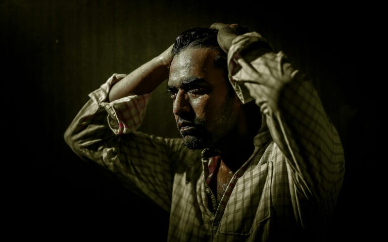 Man sweating and holding his head in distress in a dark room, illustrating the physical and psychological discomfort associated with benzodiazepine withdrawal during benzo detox.